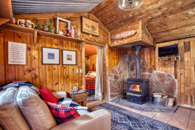 Inside view of a 1-bedroom cabin with wood-burning stove, tv and comfortable seating at Raymond Store Cabins between Lyons and Allenspark, Colorado.